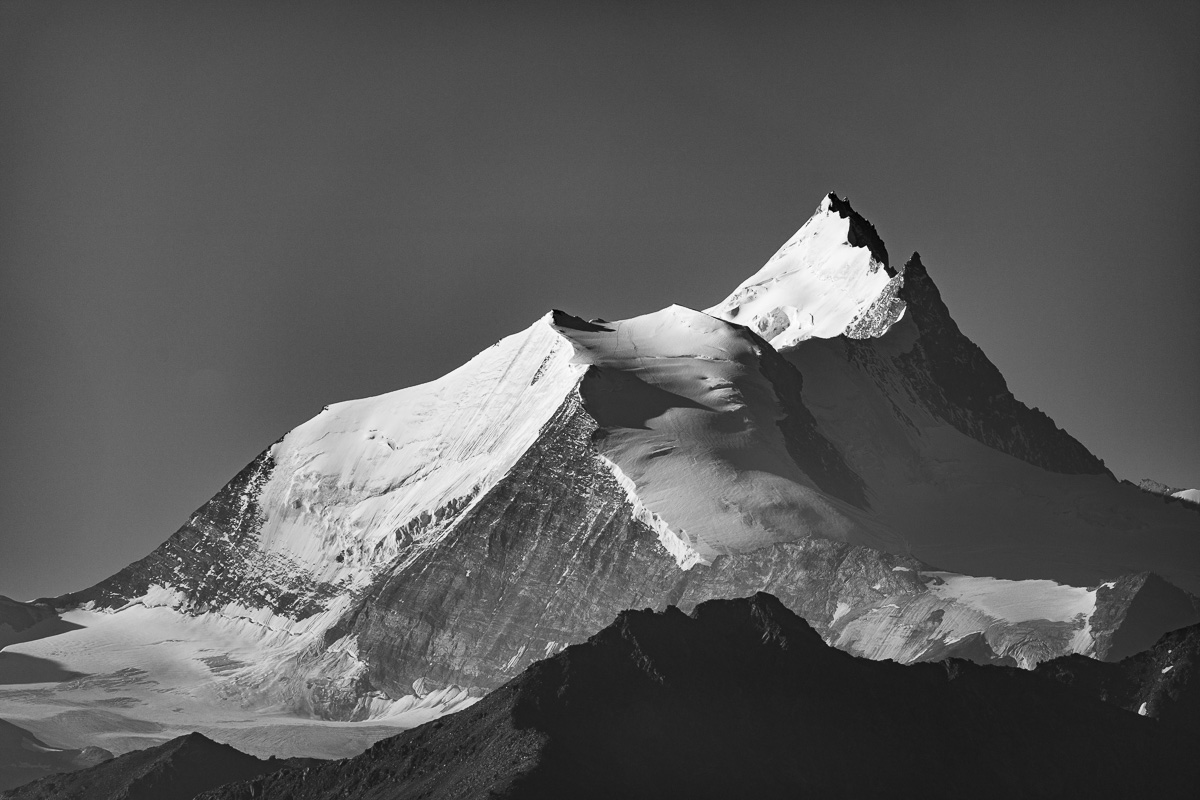 Ein in Schwarz und Weiß dargestellert schroffer schneebedeckter Berggipfel der schweizer Alpen.